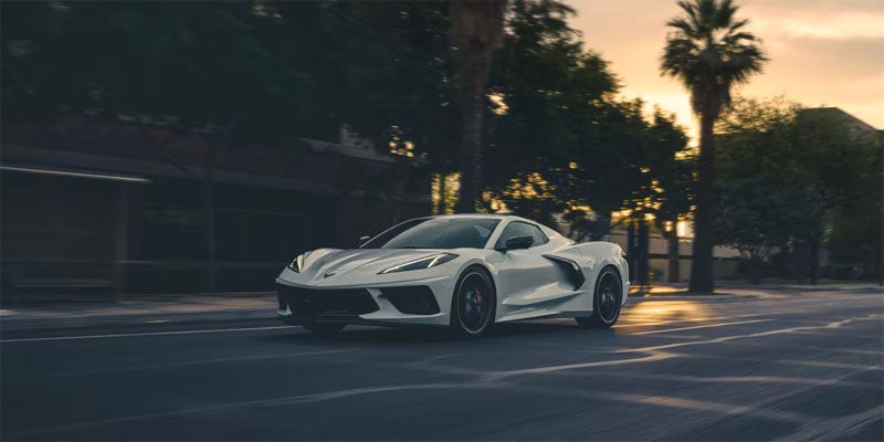 A white sports car driving on a city street at dusk