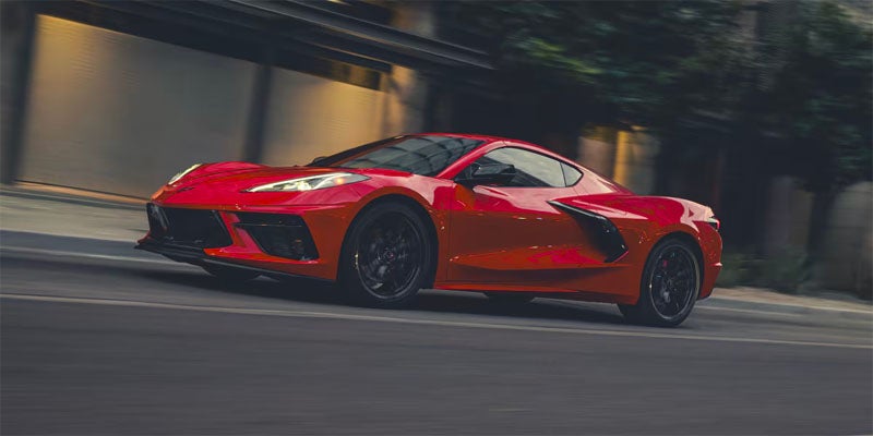 A red Chevrolet Corvette Stingray driving through a city street at night
