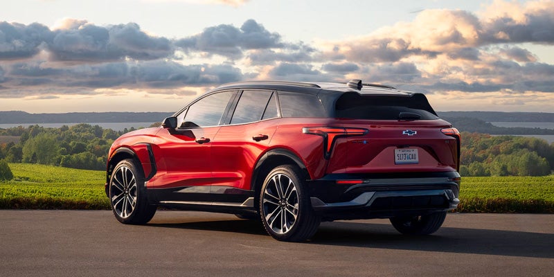 A red SUV parked on a scenic overlook with rolling green hills
