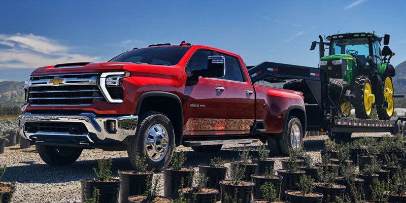 A red Chevrolet Silverado 3500 HD towing heavy farm equipment