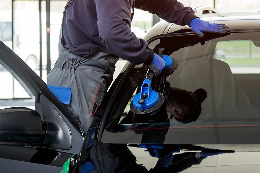 A technician installing a new windshield on a vehicle using blue suction tools